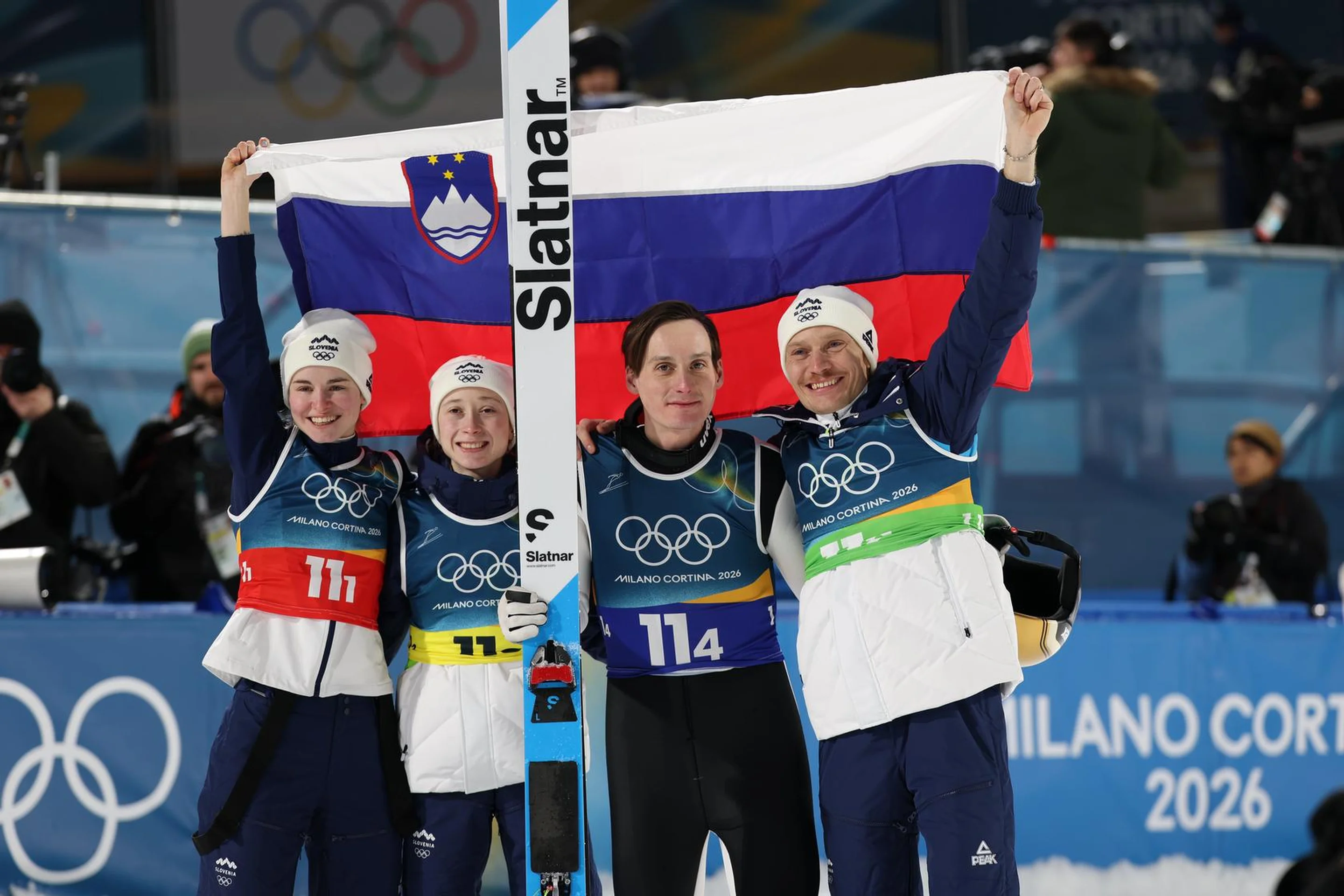 Four athletes in ski suits celebrate with a Slovenian flag at the Winter Olympics, displaying team spirit and joy.