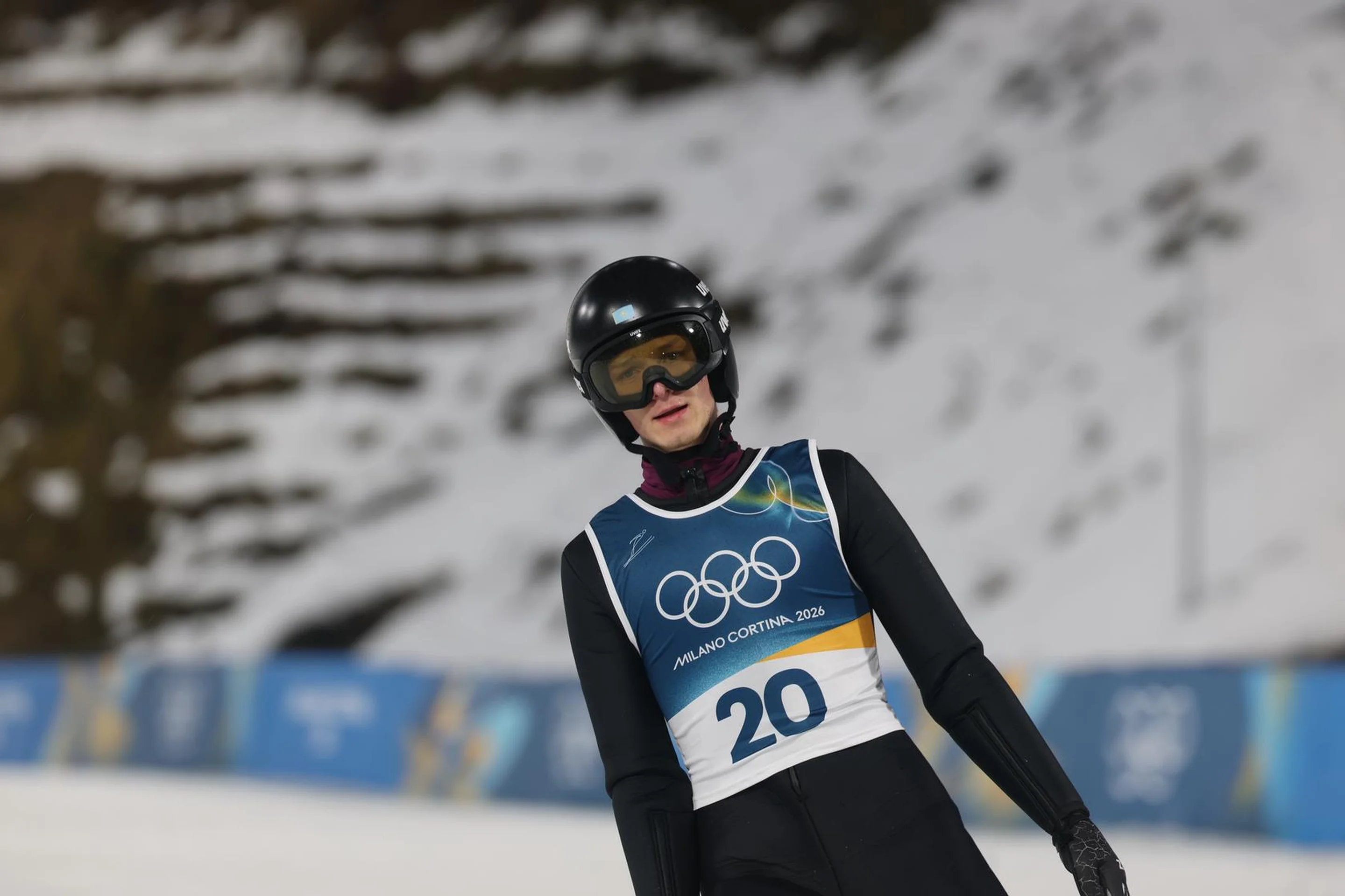 A skier wearing a helmet and bib number 20 competes on a snow-covered slope at the Milano Cortina 2026 event.