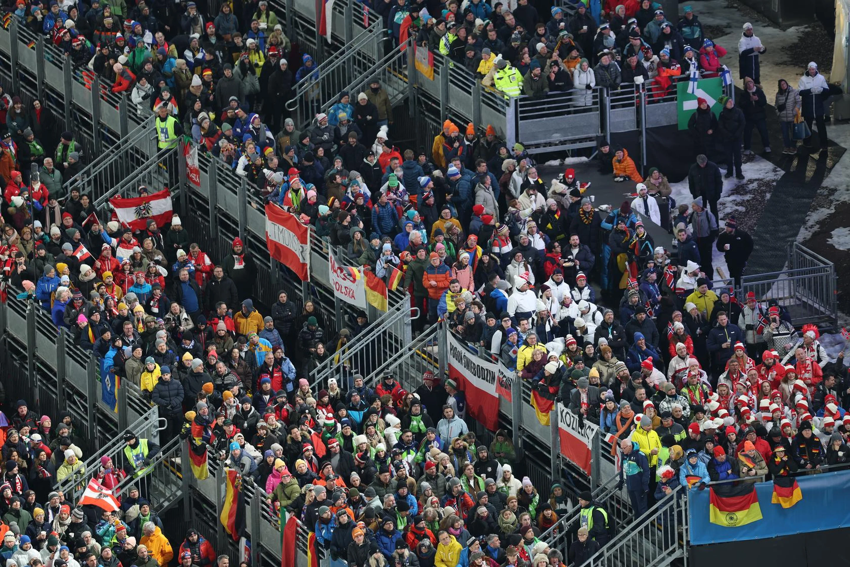 Aerial view of a colorful crowd at an outdoor event, with people holding various national flags in a stadium setting.