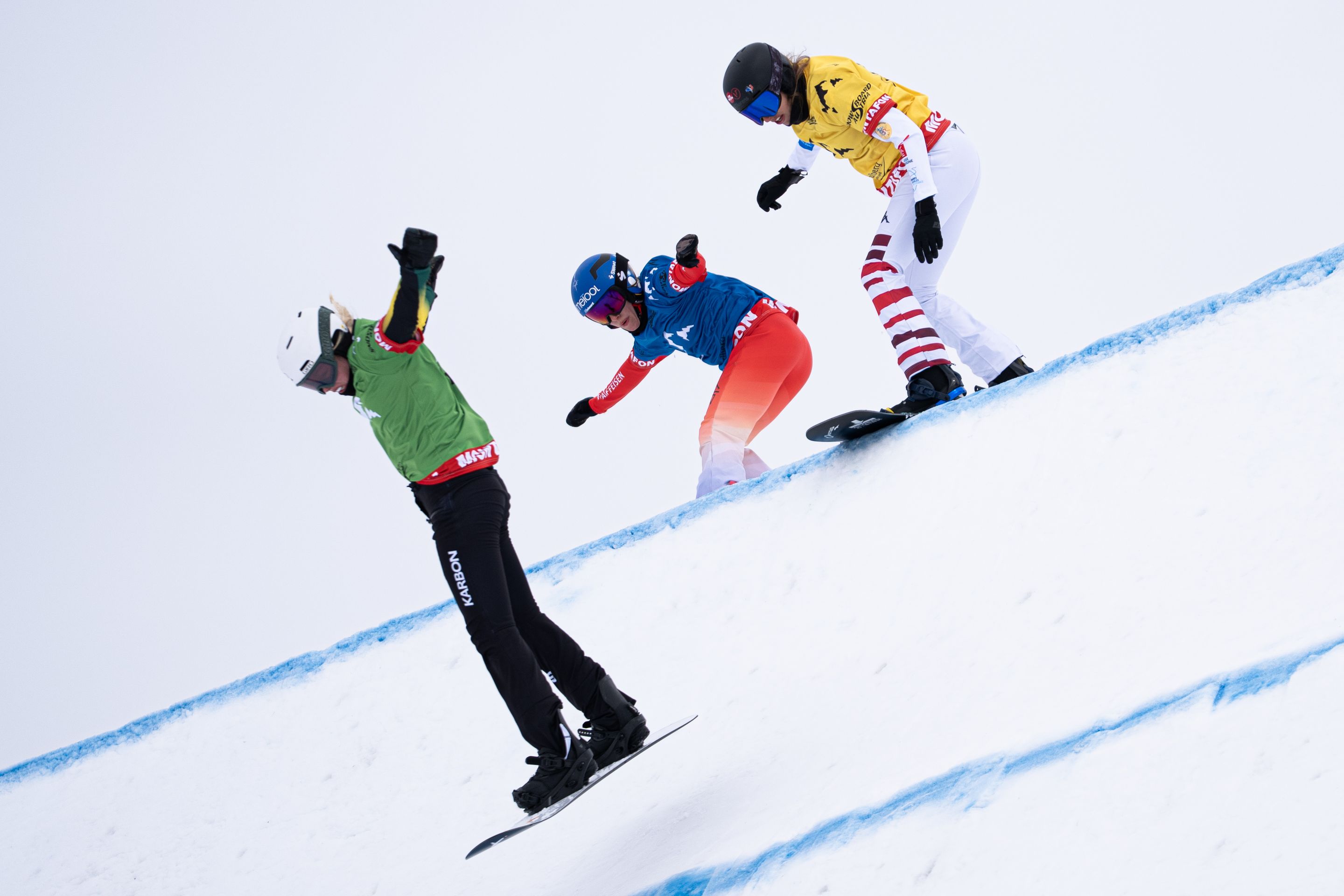 Chloe Trespeuch, in a yellow bib, racing in Montafon in March 2025. She is seen at the top of a jump, chasing two other riders in green and blue bibs