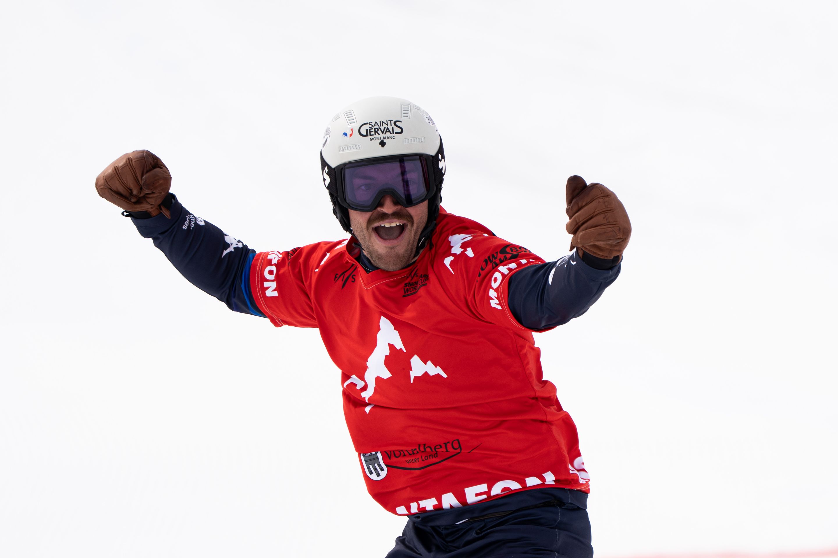 Snowboarder Loan Bozzolo in a red bib lifts his arms in the air in celebration