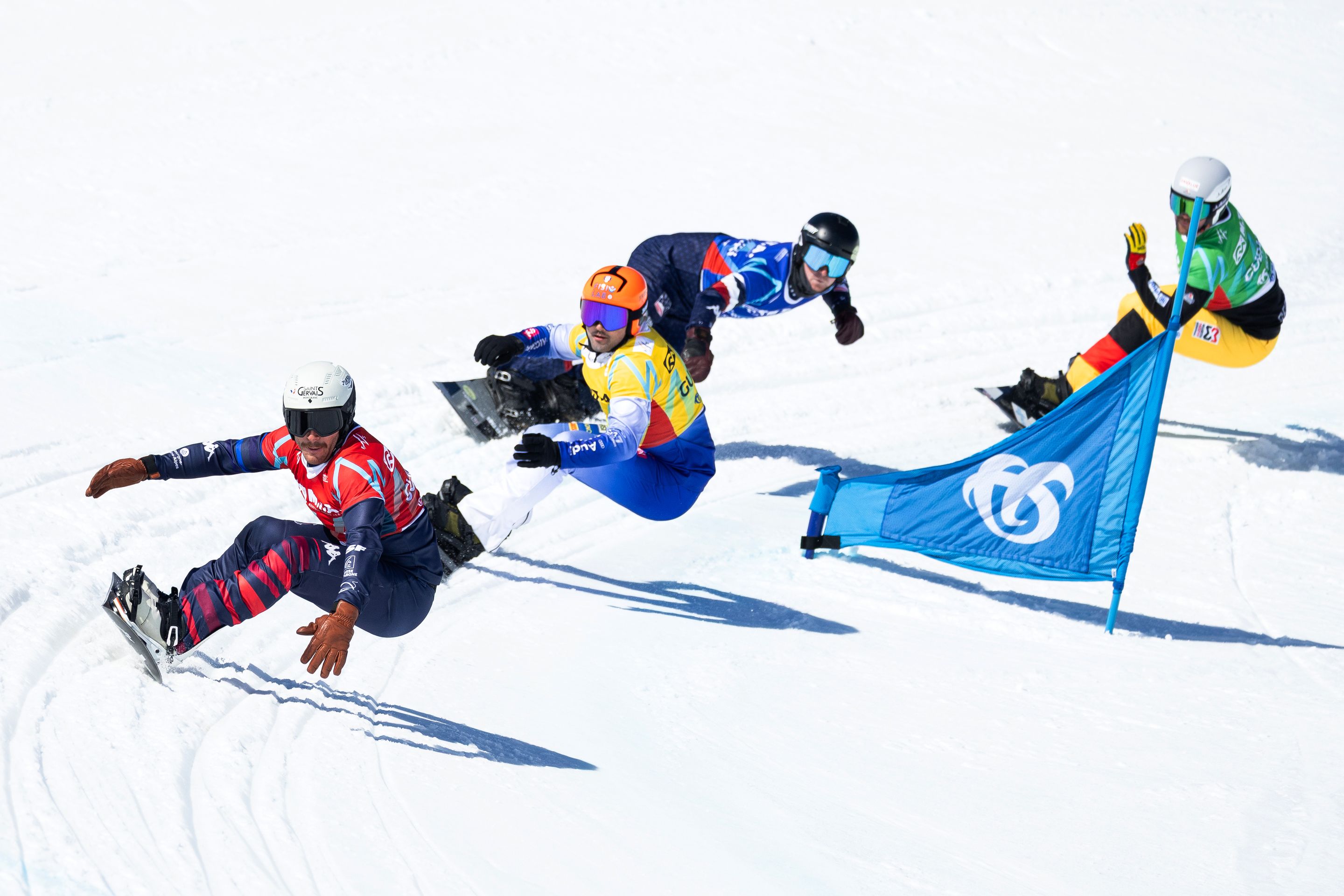 Four male snowboarders in coloured bibs take a corner during a World Cup race