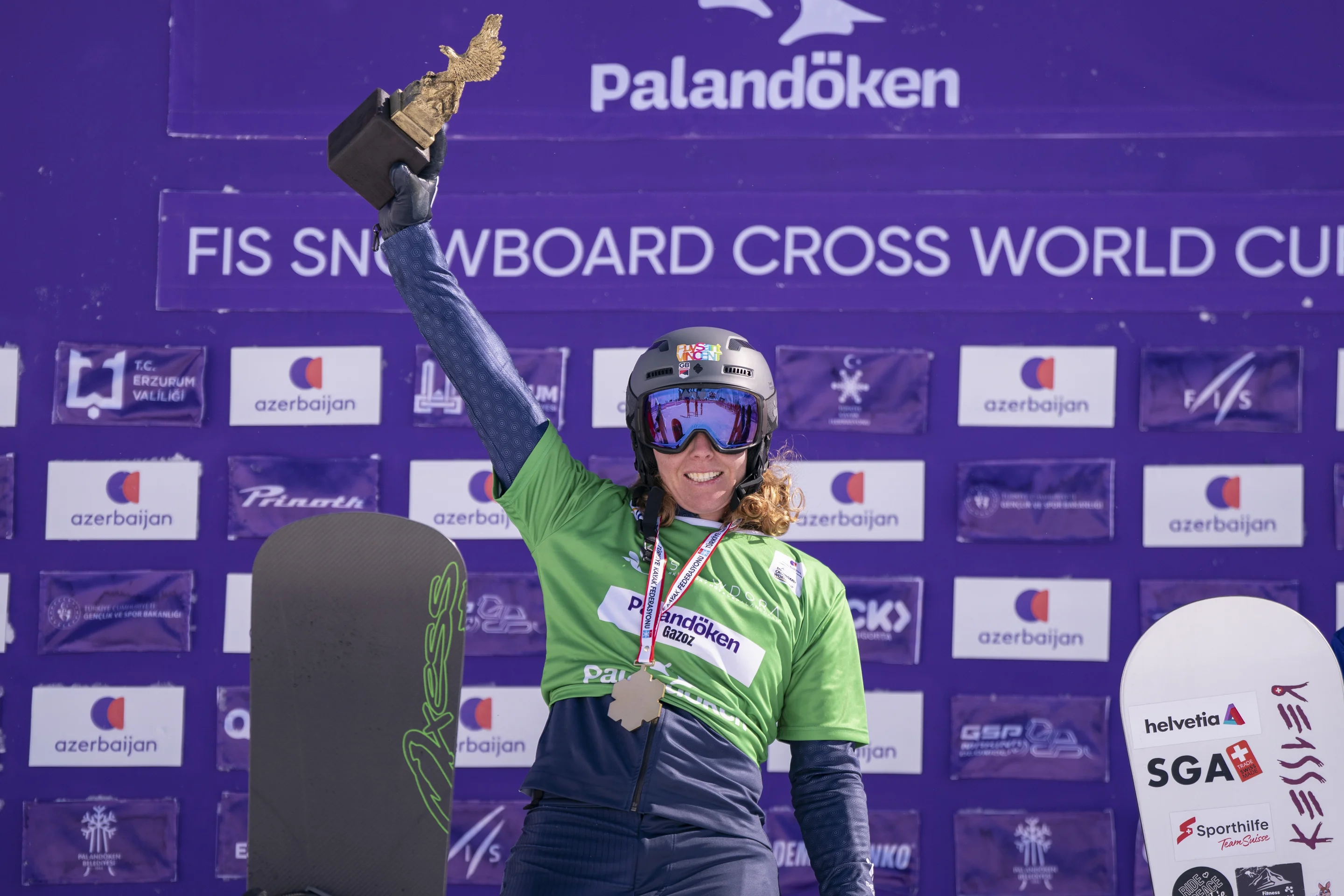 Wearing a green bib and smiling, Charlotte Bankes raises a trophy shaped like an eagle high as she celebrate her World Cup win