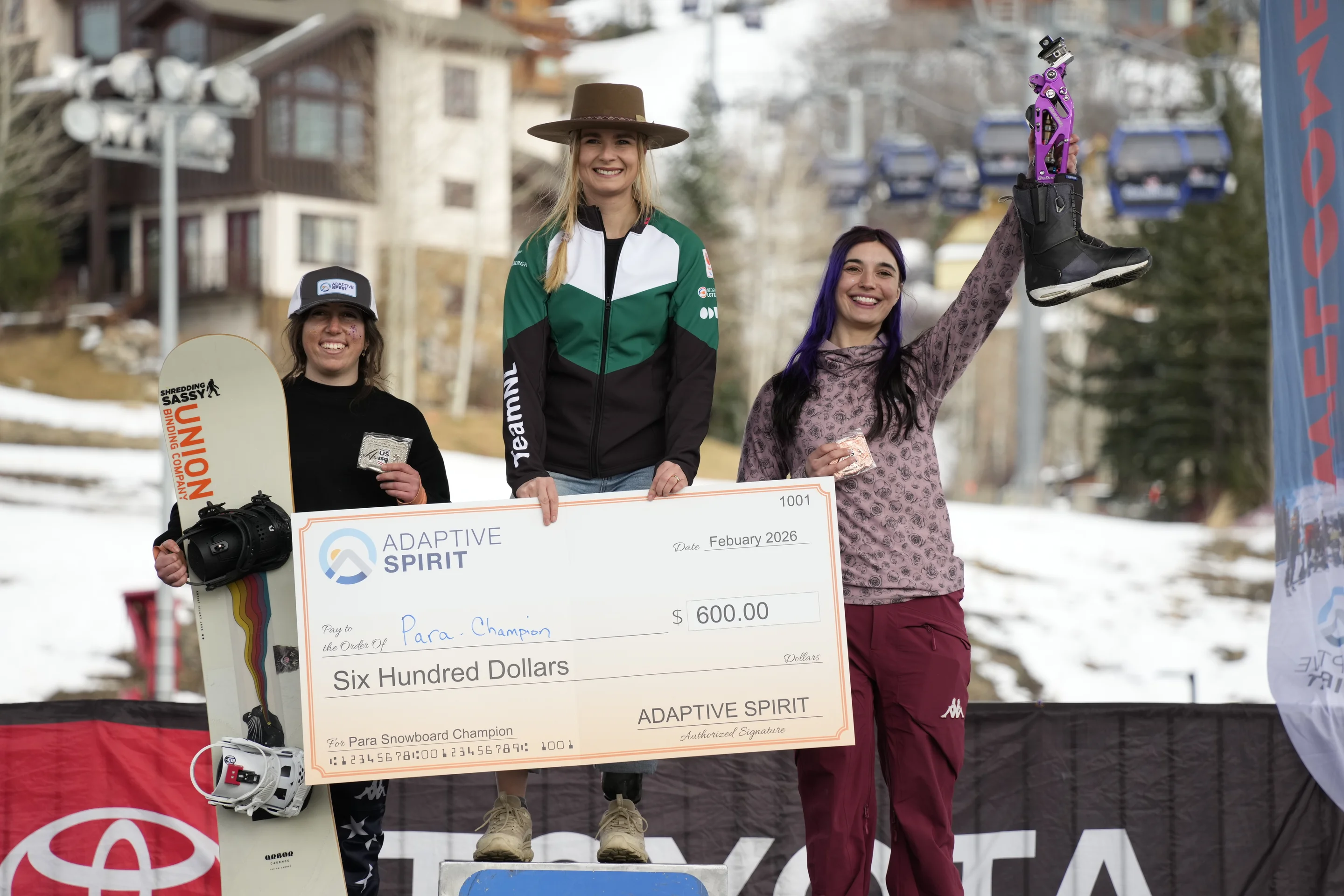 Three women on podium with winner in middle holding a cheque