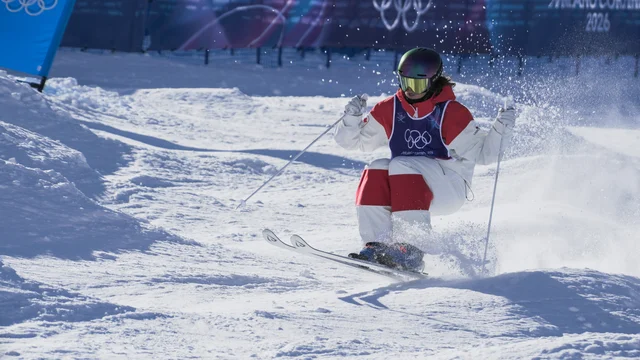 A freestyle skier in mid-air, performing a trick over a jump on a moguls course.