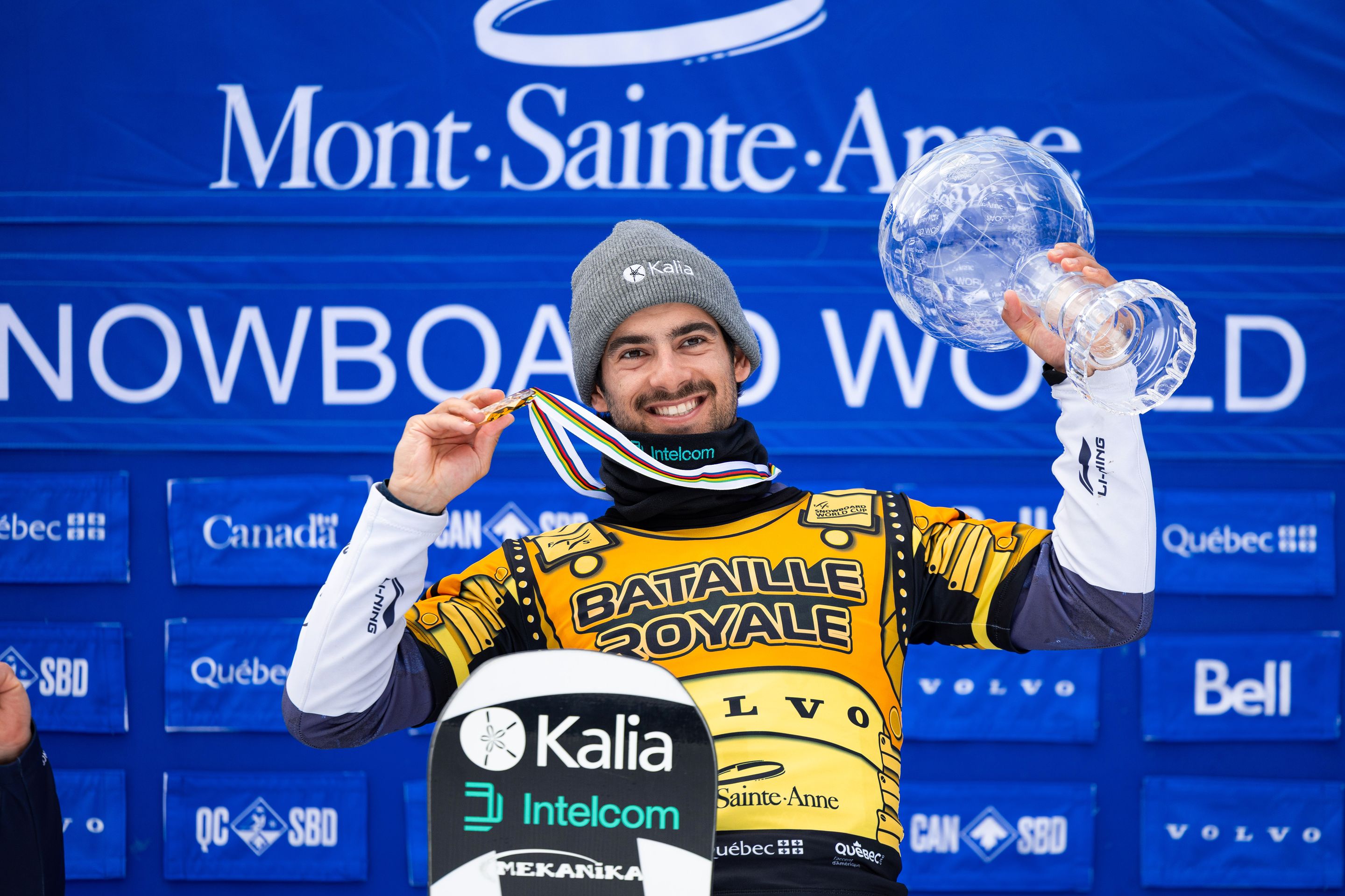 Snowboarder Eliot Grondin in a yellow bib lifts his Crystal Globe and medal at the end of the 2024/25 season