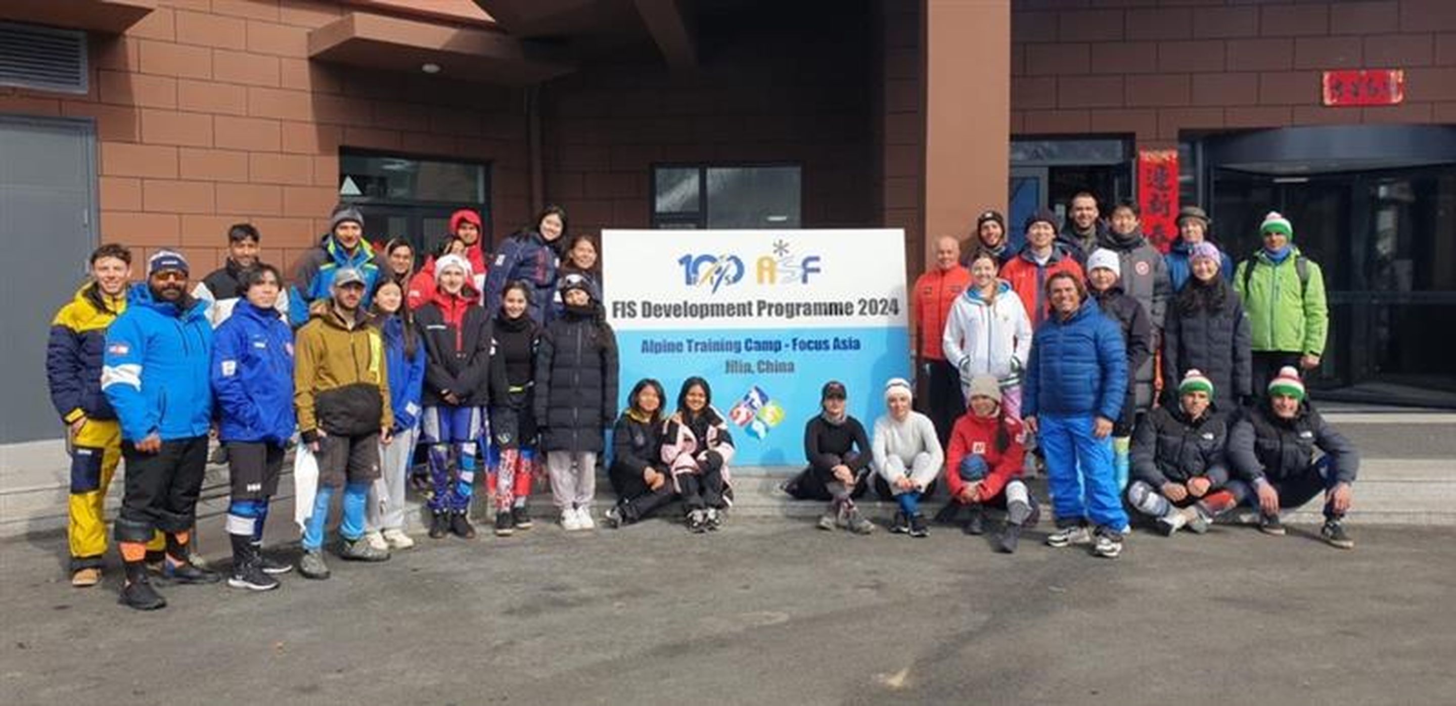 Alpine Skiing Training Camp's participants posing together around a big poster of FIS Development Programme 2024