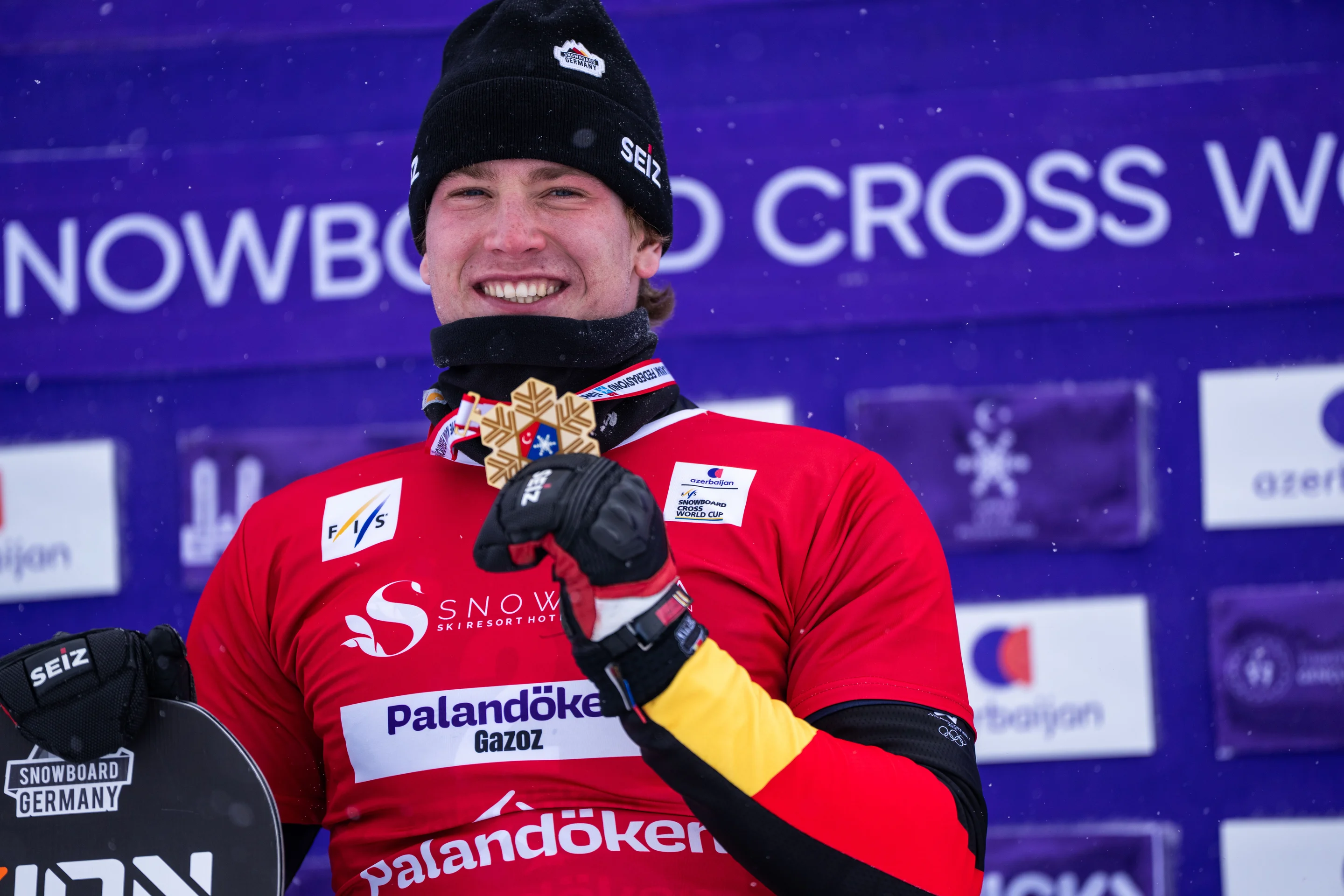 Wearing a red bib and a black beanie hat, Germany’s Leon Ulbricht lifts his World Cup medal in the air