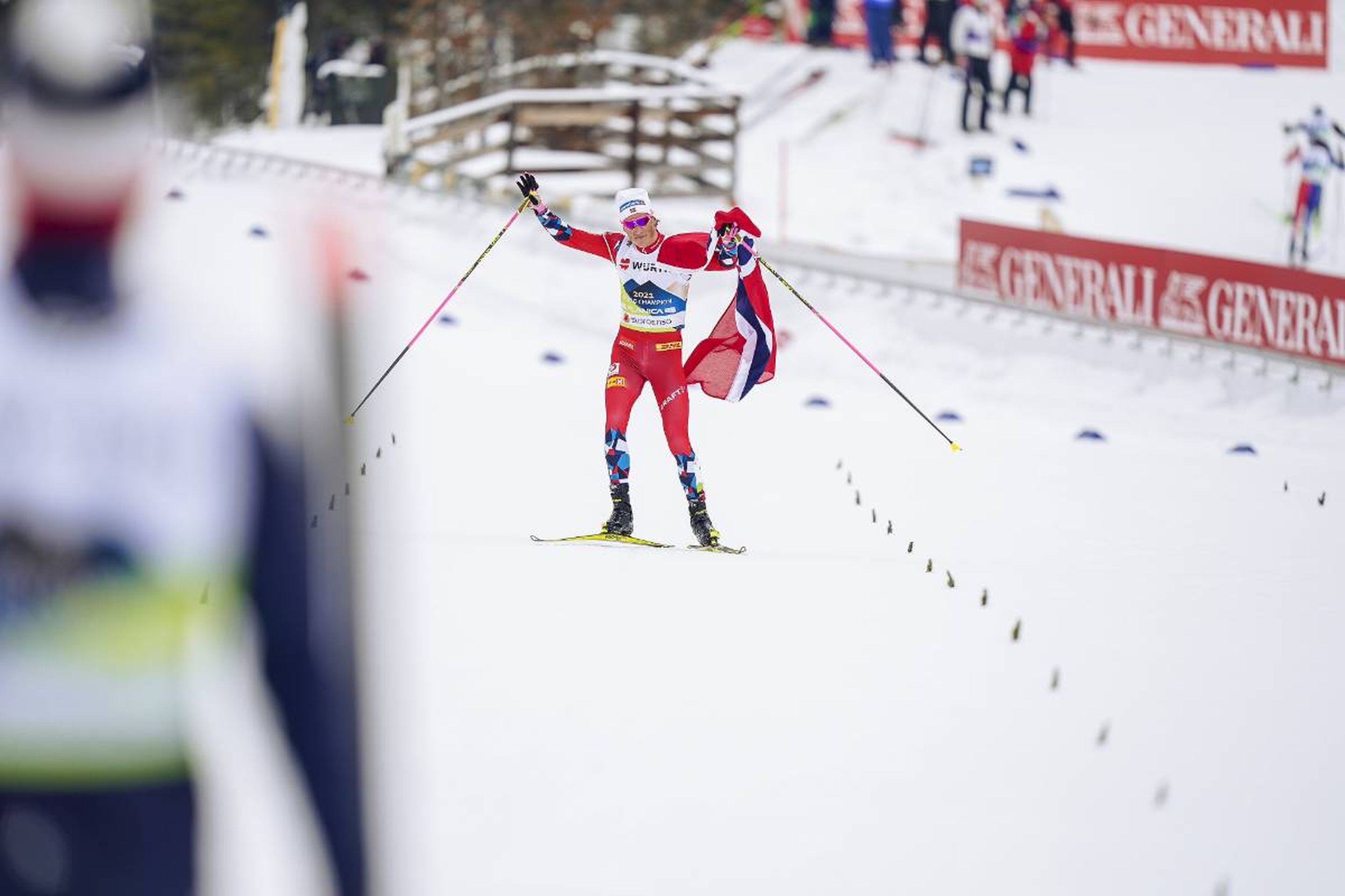 Norway's Johannes Hoesflot Klaebo celebrates with the Norwegian flag on the home straight: @Nordic Focus.